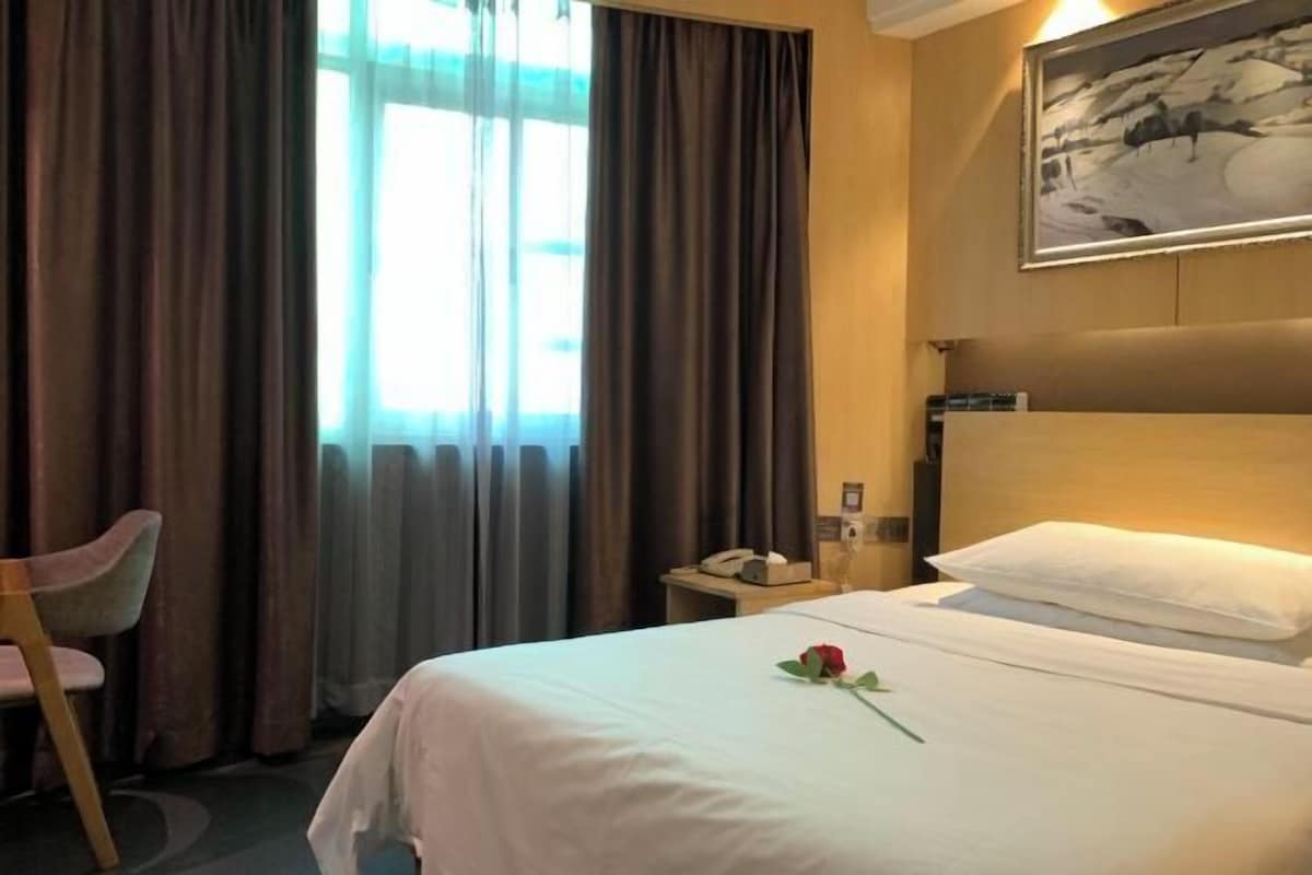 A hotel room with a bed, a chair, a painting on the wall, and a window with curtains.