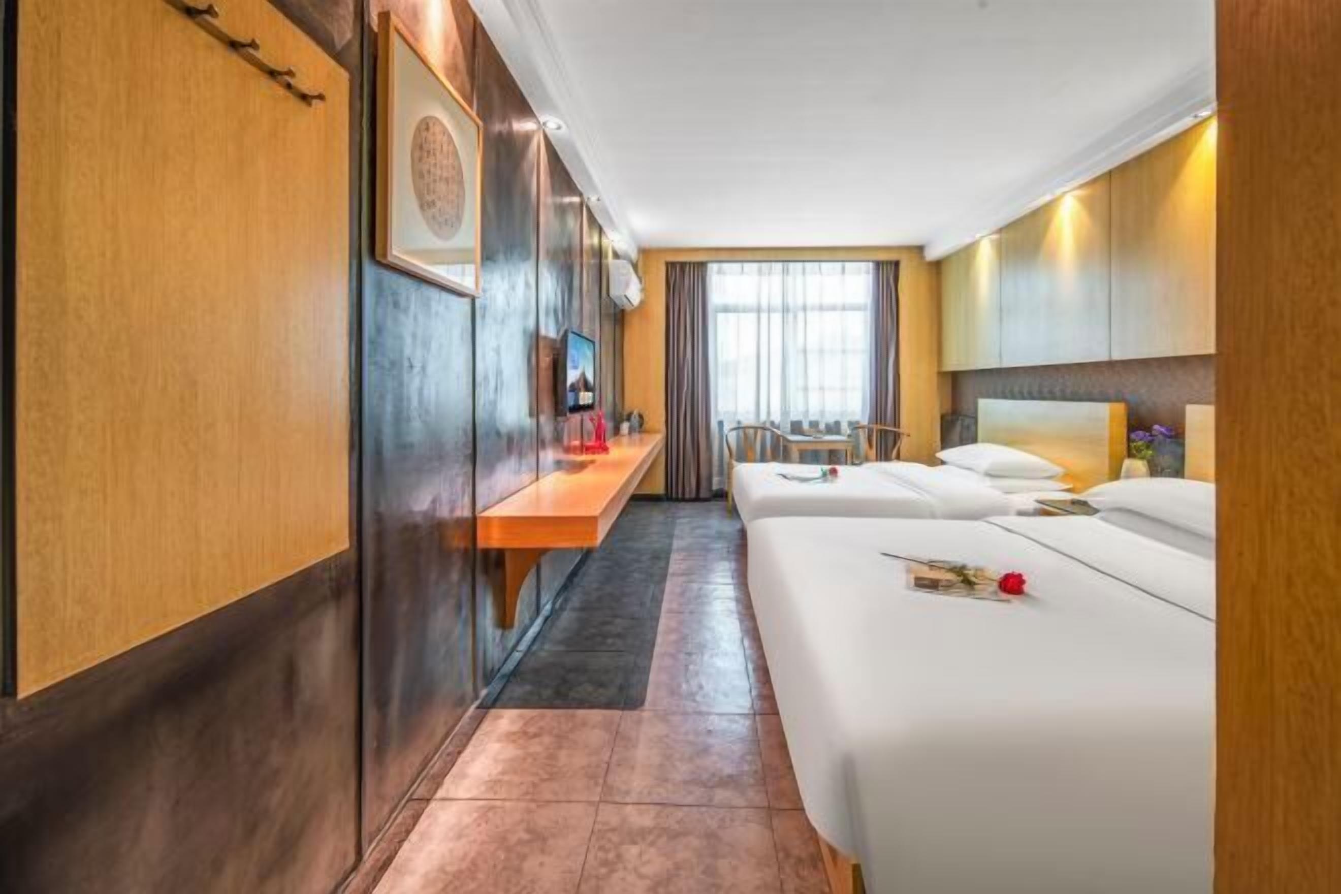 A hotel room with two beds, a desk, a TV, and a window with curtains.