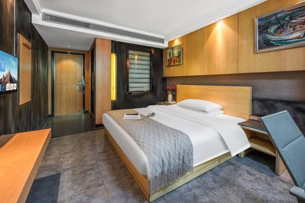 A hotel room with a large bed, a desk, a chair, a TV, and a painting on the wall.