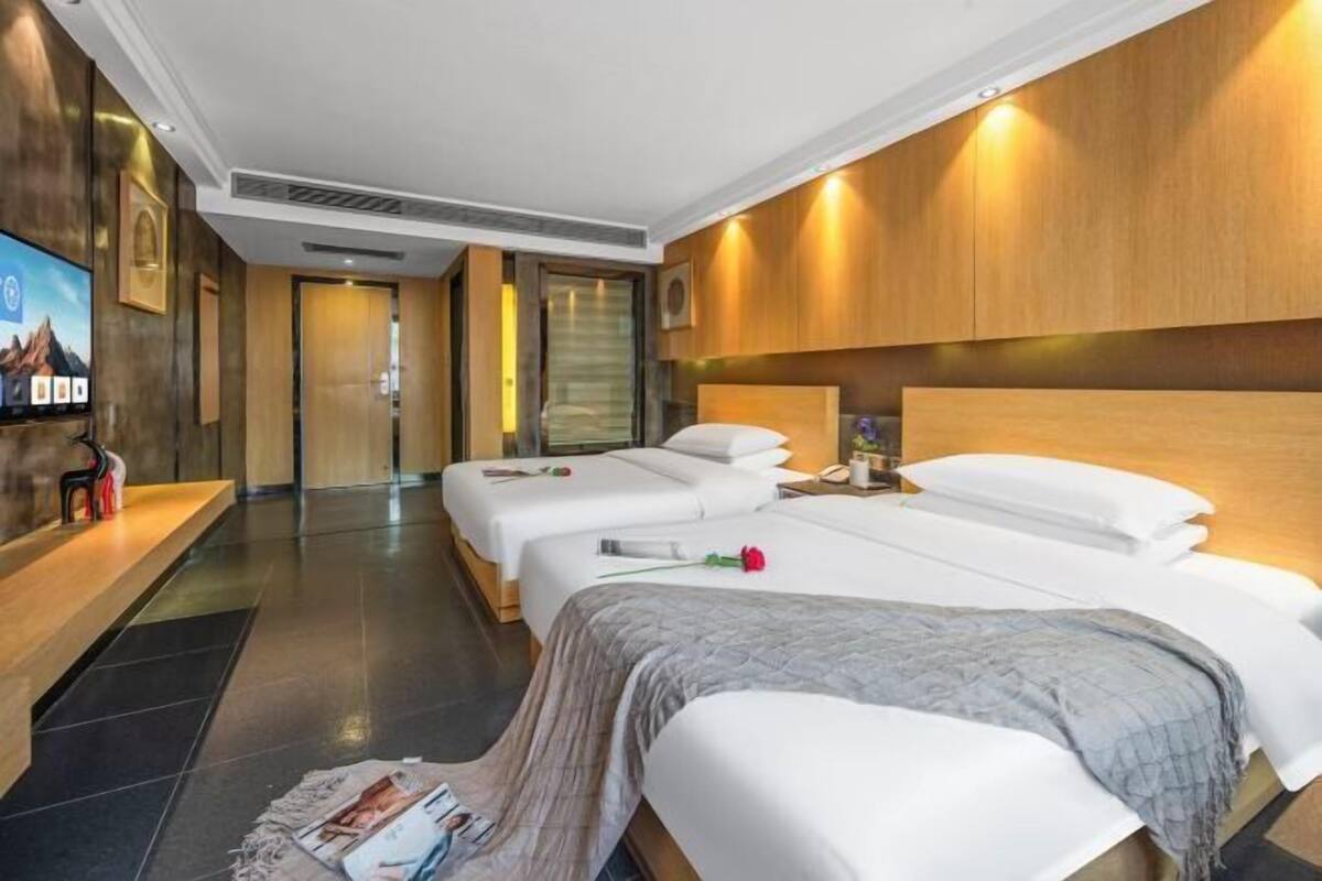 A hotel room with two beds, a TV, a wooden headboard, and a reception area.