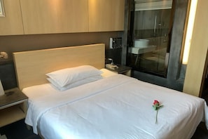A hotel room with a bed, a nightstand, a bathroom with a glass shower enclosure, and a wooden headboard. - Chenzhou Jiari Hotel (Chenzhou)