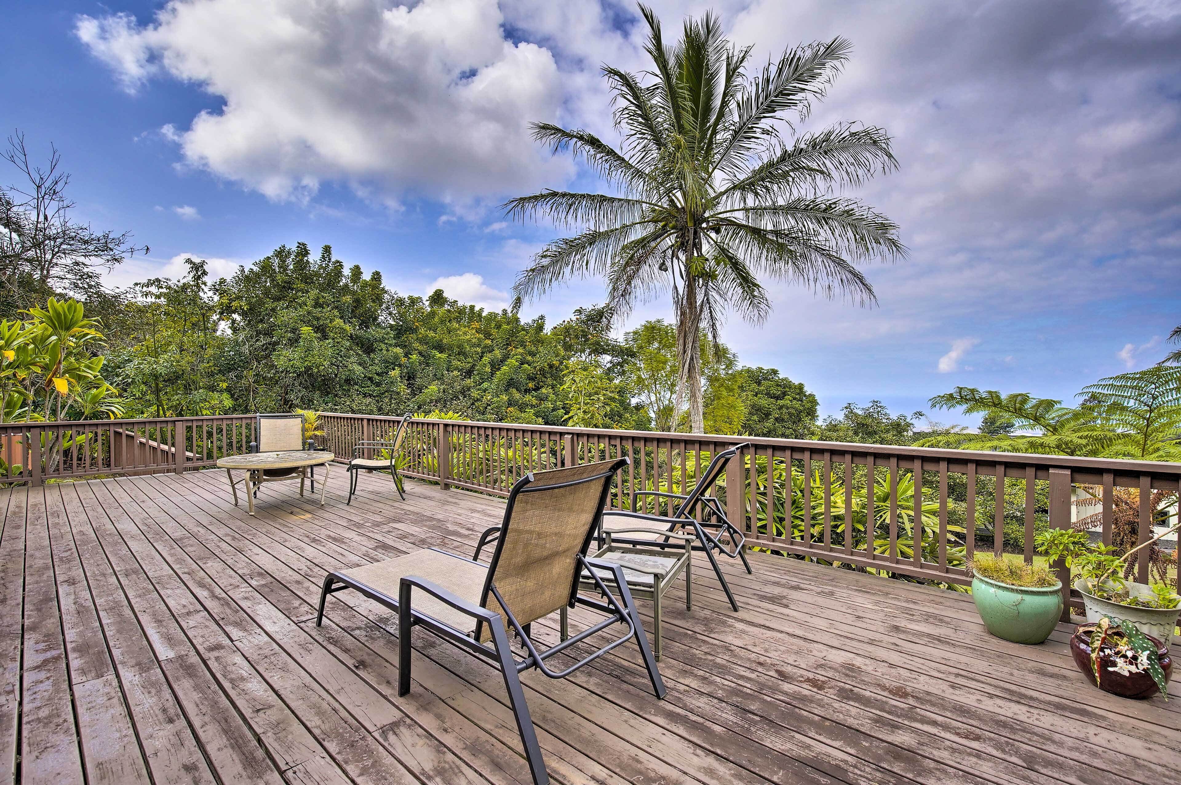 Une terrasse en bois avec des meubles d’extérieur, un palmier et une végétation luxuriante en arrière-plan.