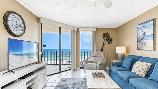 A living room with a TV, sofa, coffee table, and a view of the beach.