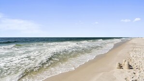 A beach with waves, a clear sky, and a few sand sculptures.