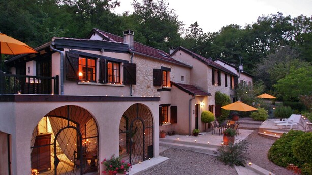 A building with a stone facade, arched windows, outdoor seating, and a fire feature.