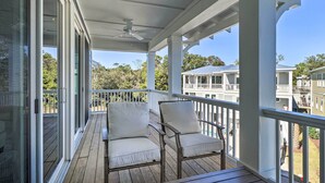 A covered porch with two cushioned chairs and a table, overlooking a residential area with houses and trees. - Kure Beach Townhome: Short Walk to the Beach! (Kure Beach)
