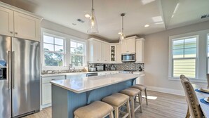 A modern kitchen with a central island, stainless steel appliances, and bar stools. - Kure Beach Townhome: Short Walk to the Beach! (Kure Beach)