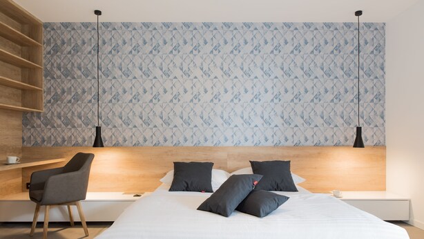 A modern bedroom with a bed, a chair, a shelf, and a patterned wall. - BCAdria apartment Deluxe (Split)