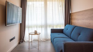 A modern room with a blue sofa, a small round table with a cup, and a TV mounted on the wall. - BCAdria apartment Deluxe (Split)