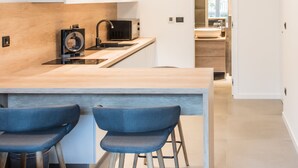 A modern kitchen with a wooden countertop, a built-in microwave, and a pendant light. There are two blue bar stools and a wooden table. - BCAdria apartment Deluxe (Split)