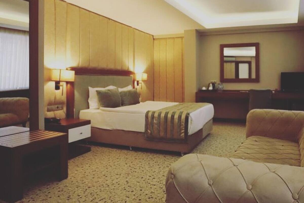 A hotel room with a large bed, a desk, a chair, a television, and a mirror.