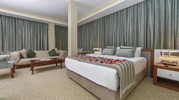 A hotel room with a large bed, a sofa, a coffee table, and a nightstand.