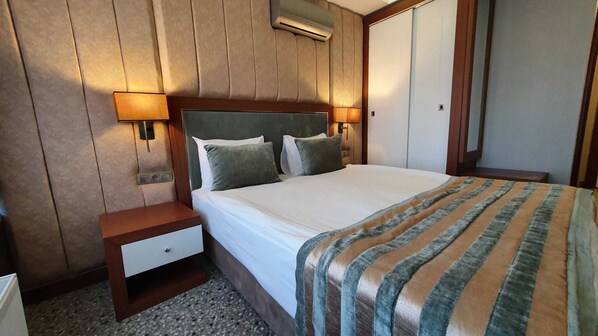 Quarto de hotel com cama, mesa de cabeceira, gaveta, ar-condicionado fixado na parede e duas luminárias.