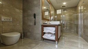 A modern bathroom with a toilet, a sink with a mirror, a glass shower enclosure, and a towel rack. - Royal Sweet Hotel (Ankara)