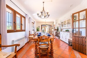 Uma sala de jantar com uma mesa de madeira posta para quatro pessoas, um lustre e vista para o jardim através de grandes janelas.