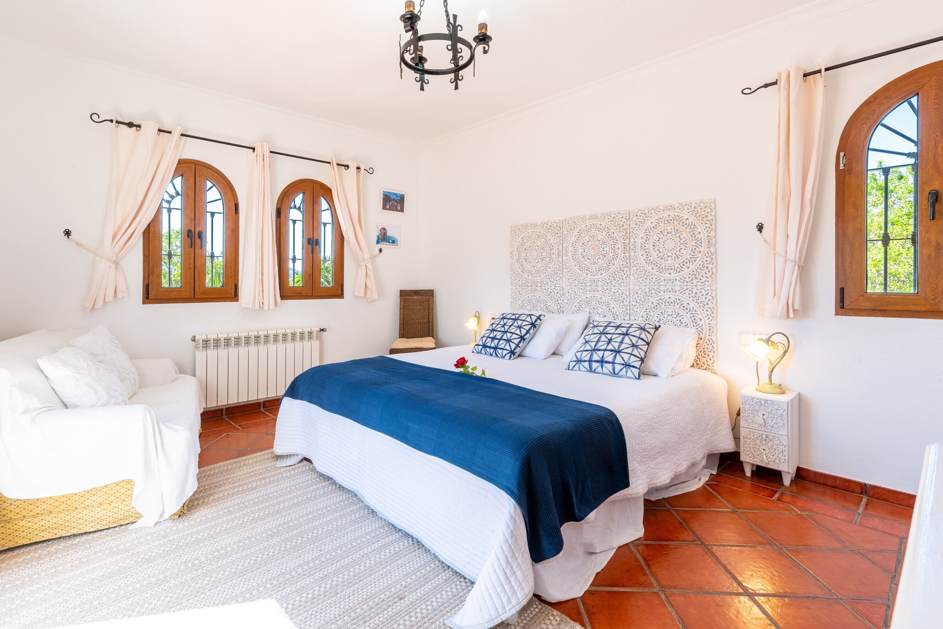 A bedroom with a bed, a nightstand, a chair, a radiator, and a window with curtains.