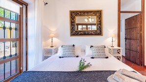 Une chambre à coucher avec un grand lit, deux tables de chevet, un miroir et une vue par la fenêtre.