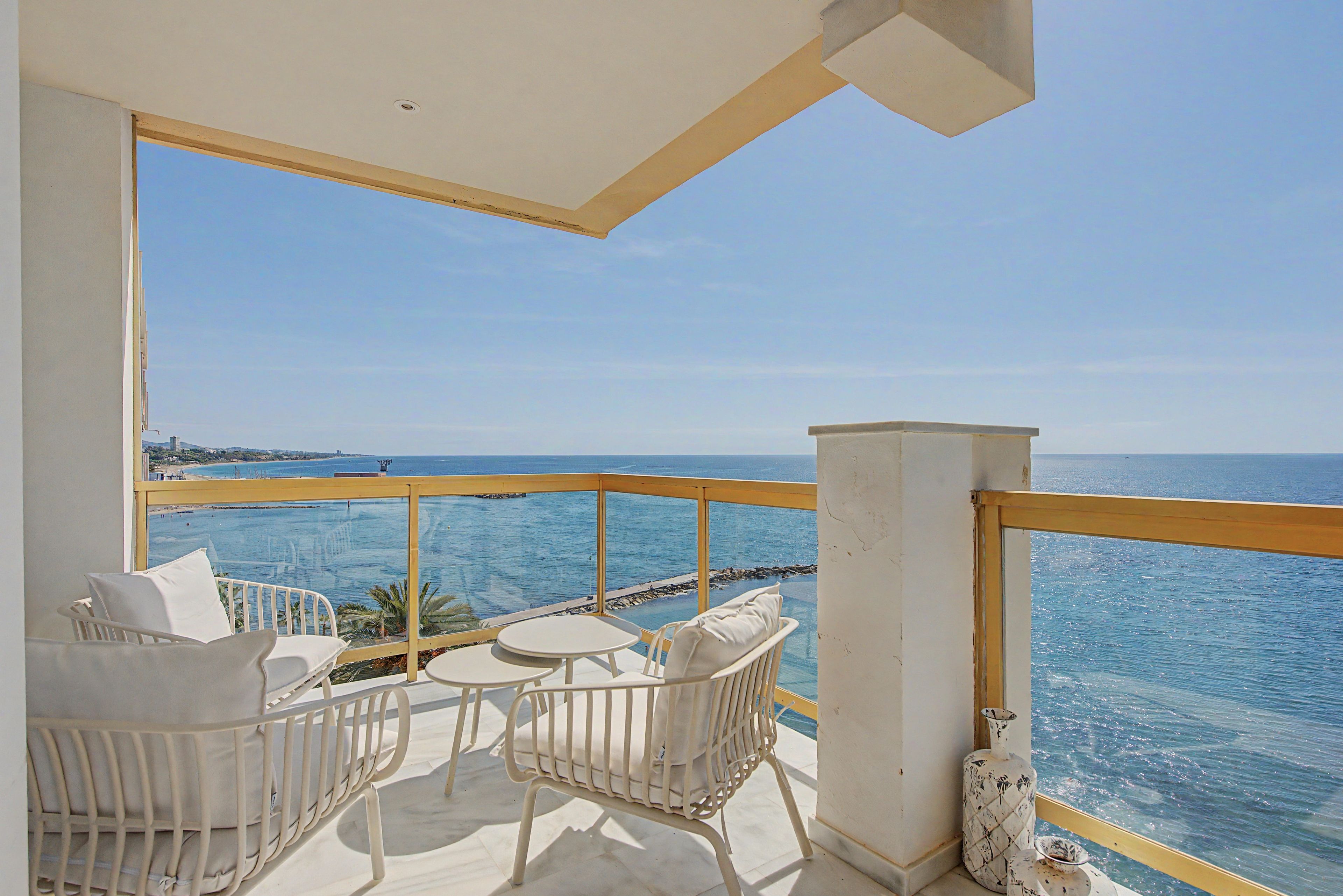 Ein Balkon mit weißer Möbel, Blick auf das Meer und einem klaren Himmel.
