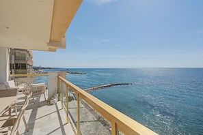 A balcony with a view of the sea, a wooden railing, and outdoor furniture.