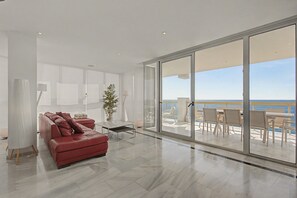 A modern living room with a red sofa, a glass table, and a view of the sea through large sliding doors. - Unique beachfront apartment with spectacular sea views, pool, Wi-Fi, and terrace (Marbella)
