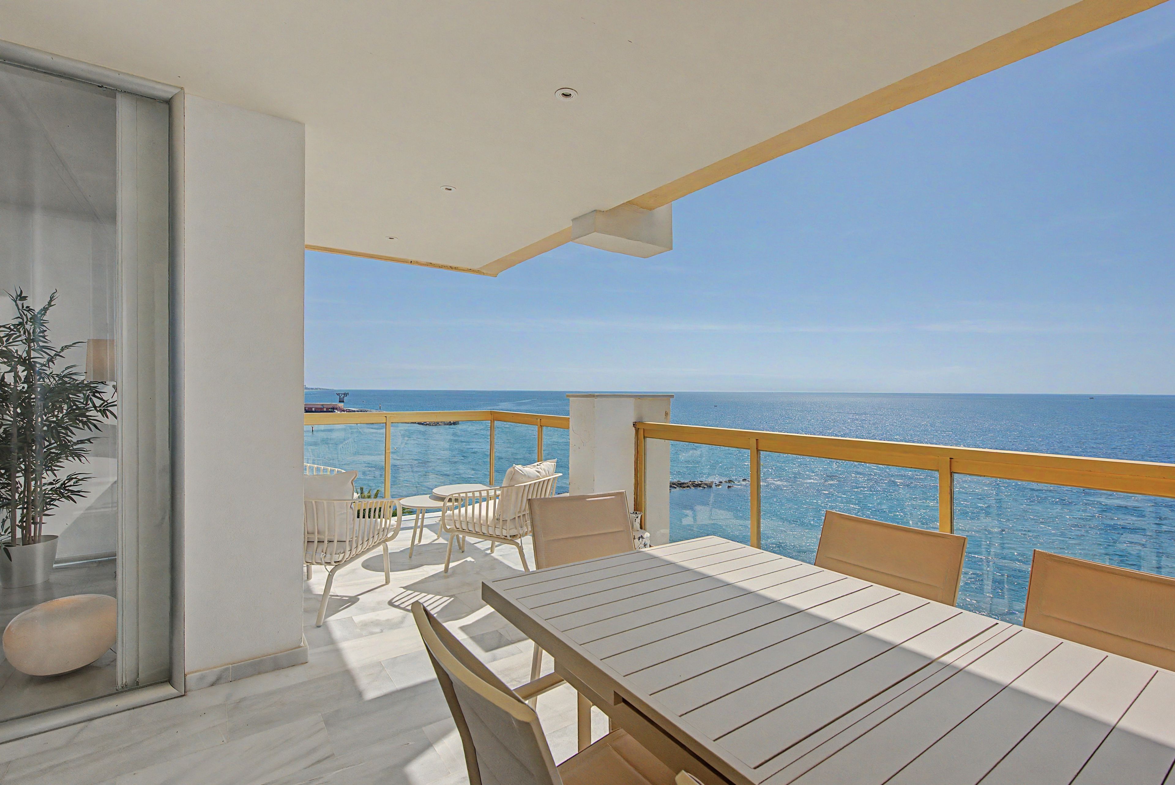 A balcony with a table and chairs, overlooking a body of water.