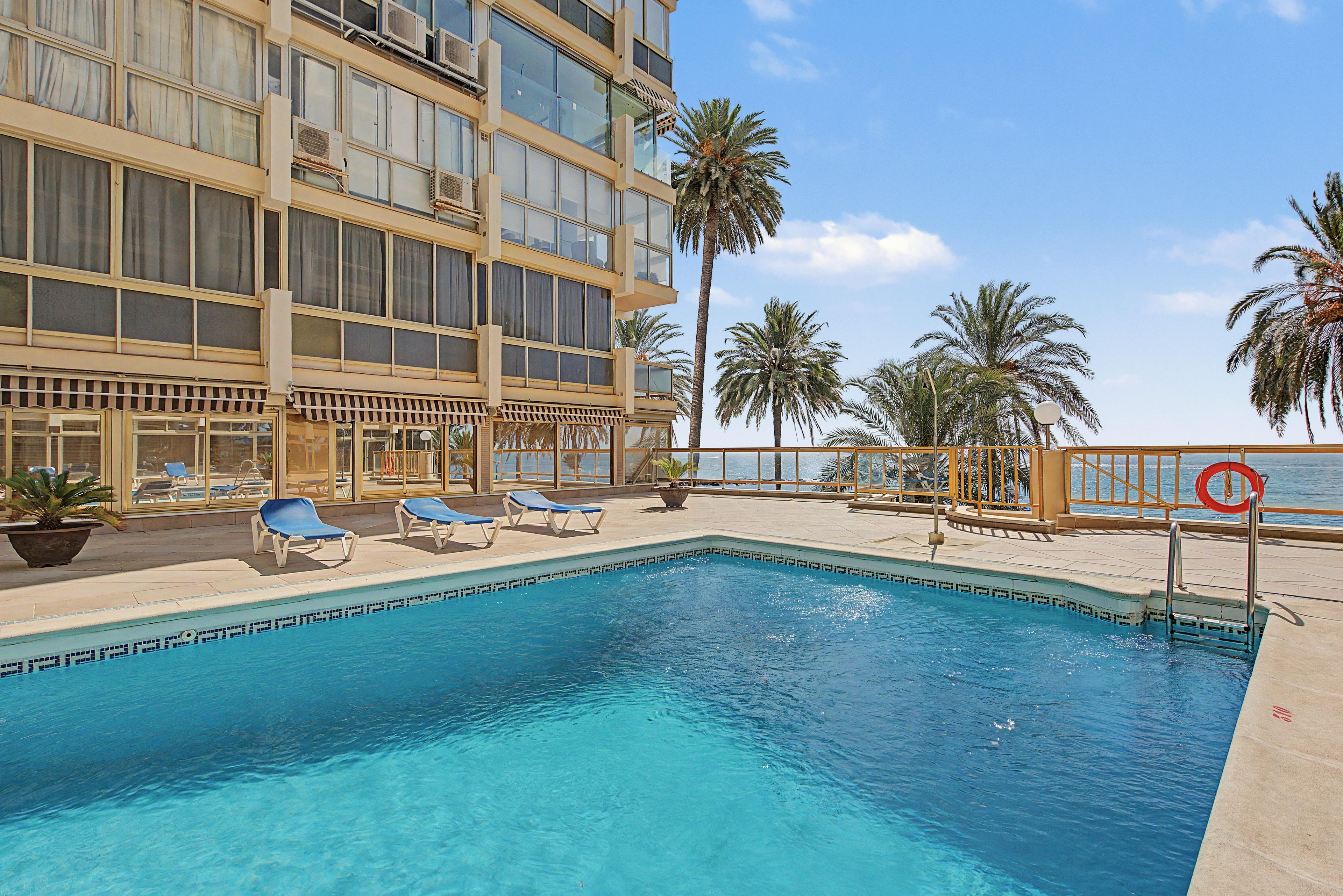 A pool area with lounge chairs, a lifebuoy, and a view of the ocean.