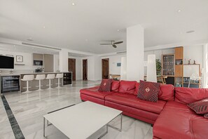 A modern living room with a red leather sofa, a white coffee table, and a kitchen area with a microwave and bar stools. - Unique beachfront apartment with spectacular sea views, pool, Wi-Fi, and terrace (Marbella)