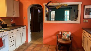 Una cocina con armarios blancos, una pared roja, un ventanal con vistas y una silla con un cojín colorido.