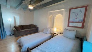 Un dormitorio con dos camas, un sofá, una lámpara y un cuadro en la pared.