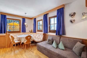 A cozy room with a wooden bench, a sofa, a table, and large windows with curtains.