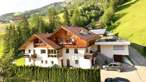 A two-story chalet with a wooden exterior, a balcony, and a car parked in front.