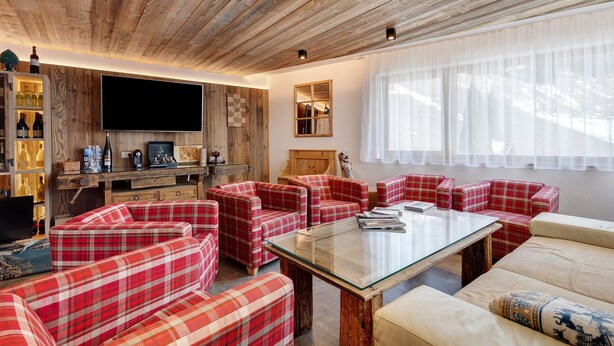 A living room with red plaid sofas, a glass coffee table, wooden ceiling, and a TV.
