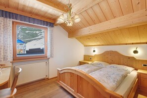 A wooden bedroom with a bed, bedside tables, a window with a view, and a ceiling light fixture.