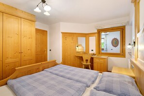 A bedroom with a bed, wooden wardrobe, desk, chair, and a mirror.