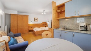 Habitación pequeña con cama, sofá, mesa de comedor, zona de cocina y armario de madera.