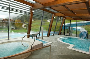 Une piscine intérieure dotée d’un jacuzzi, d’un toboggan et offrant une vue sur un paysage montagneux grâce à de grandes fenêtres.