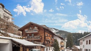 Un chalet en bois doté de balcons, un télésiège en arrière-plan et une montagne à l’horizon.