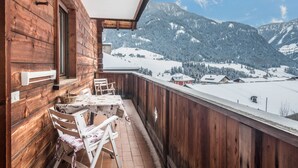 Un balcon en bois avec une table et des chaises, donnant sur un paysage montagneux enneigé.