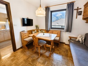 A cozy room with a wooden dining table, bench seating, a television, and a window with a view of a house.