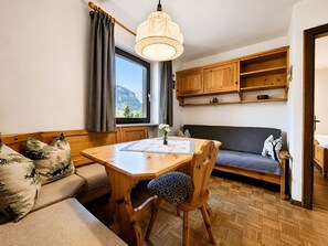 A cozy room with a wooden dining table, a sofa, a wooden cabinet, and a window with a view of mountains.