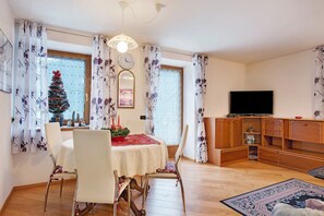 A dining area with a table set for two, a television, and a wooden cabinet.