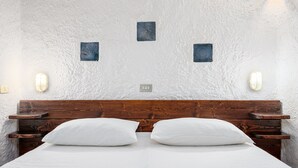 A bedroom with a wooden headboard, two white pillows, a white bedspread, and wall-mounted light fixtures.