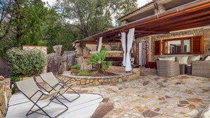 A stone patio with lounge chairs, a stone wall, and a covered area with wicker furniture.