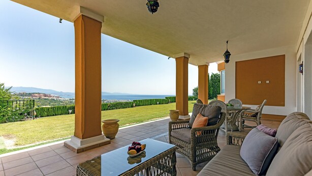 Un espacio al aire libre techado con mobiliario de mimbre, una mesa con fruta y vistas al paisaje.