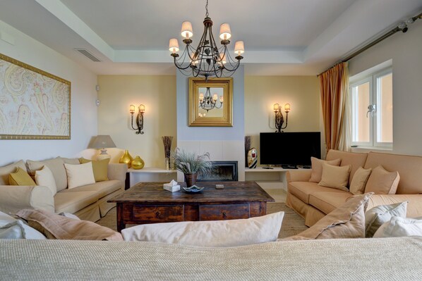 A living room with a fireplace, sofa, coffee table, and chandelier.