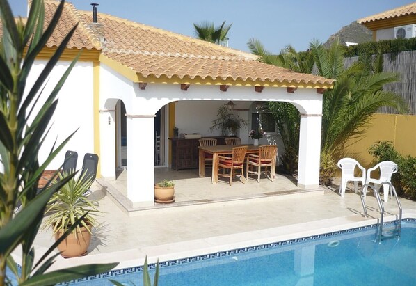 A poolside area with a covered patio, outdoor seating, and a pool.