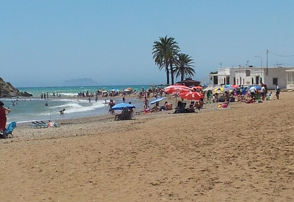 A beach with people, umbrellas, and palm trees.