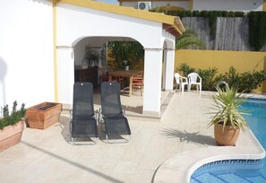 A poolside area with lounge chairs, a table, and a potted plant.
