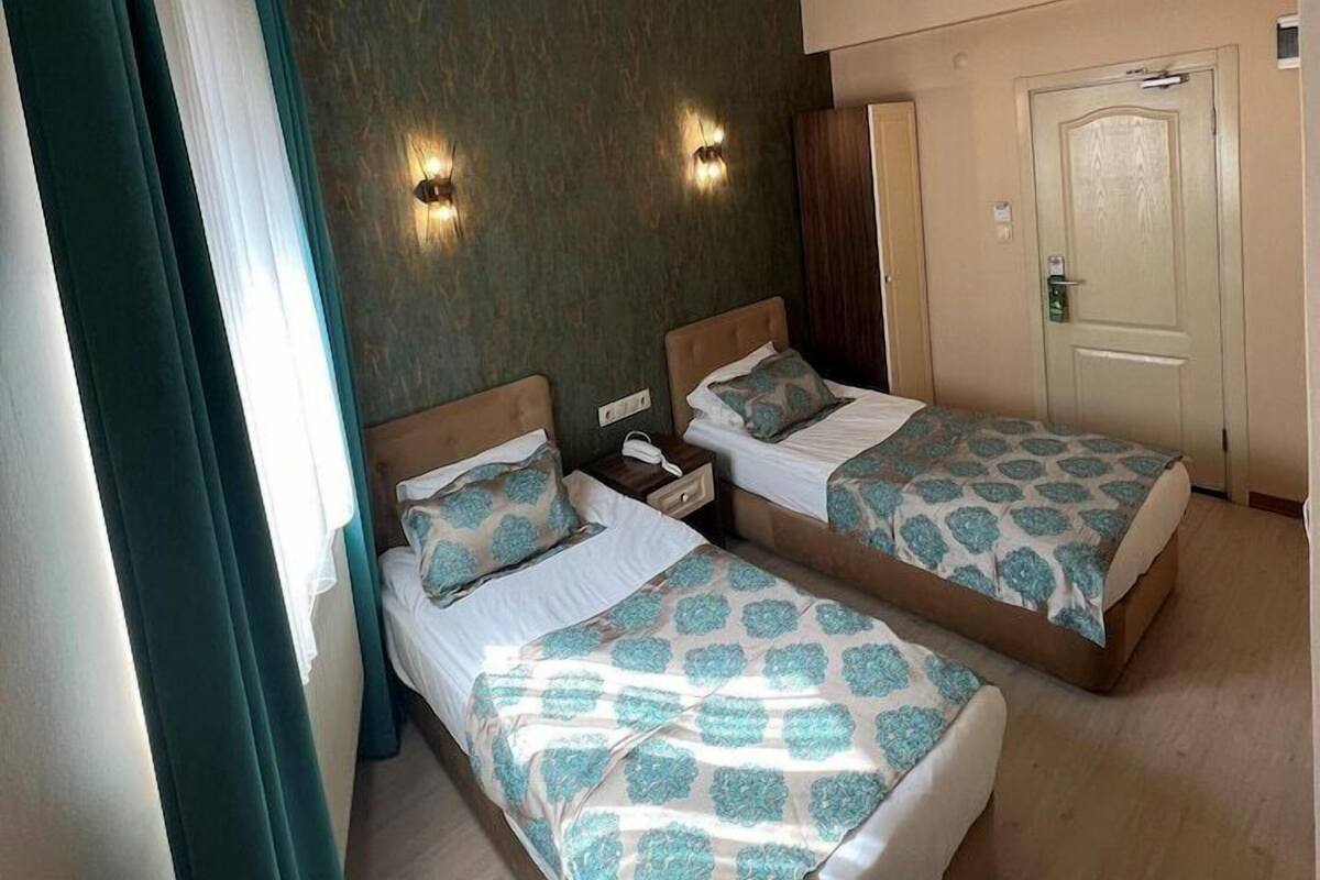 A hotel room with two beds, a wooden floor, a green accent wall, and a door.