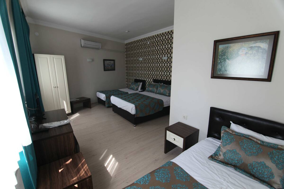 A hotel room with two beds, a desk, a chair, a wardrobe, and a painting on the wall.